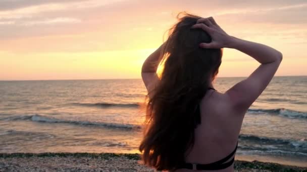 Menina na moda em um maiô preto entra no mar ao pôr do sol. Estou feliz com o mar e a praia. A experimentar a liberdade. Vai para a água. — Vídeo de Stock
