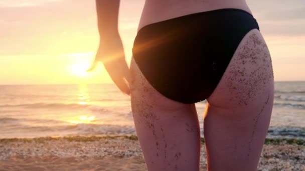 Rückansicht schöne junge Mädchen Strand Sand aus Arsch Zeitlupe tragen String Bikini sexy Po tropischen Urlaub Nahaufnahme. Mädchen schüttelt bei Sonnenuntergang den Arsch aus dem Sand. — Stockvideo