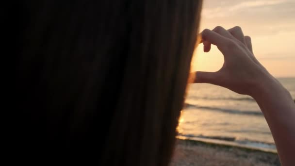 Ağır çekim, Close Up: tanınmayan kadın kalbi ile ayar güneş yakalamak parmak şeklinde. Genç kız aşk elleri altın gökyüzü çarpıcı karşı ve sabah güneş yükselen sembolü yapma — Stok video