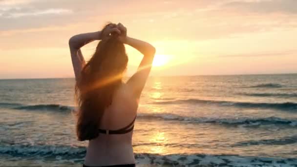 Μόδας κορίτσι σε ένα μαύρο μαγιό μπαίνει στη θάλασσα στο ηλιοβασίλεμα. Είμαι χαρούμενος με τη θάλασσα και την παραλία. Αντιμετωπίζετε την ελευθερία. Μπαίνει το νερό — Αρχείο Βίντεο