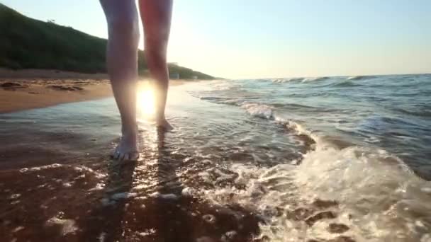 Menina andando ao longo da borda das águas. Uma mulher a percorrer a costa na areia. A câmara está a mover-se atrás da fêmea . — Vídeo de Stock