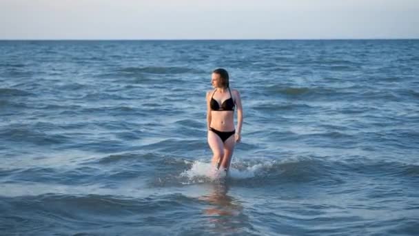 Belle femme en bikini sortant de l'océan au ralenti. fille sexy habillée dans un maillot de bain noir . — Video