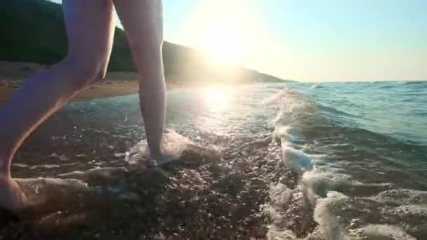 Mädchen, das entlang der Wasserkante geht. Frau, die auf Sand am Ufer entlang geht. die Kamera fährt dem Weibchen hinterher. — Stockvideo