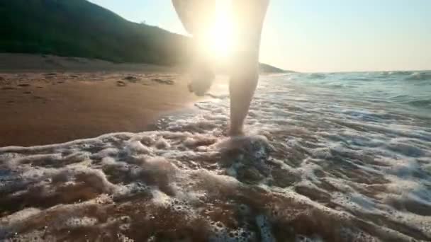 Menina andando ao longo da borda das águas. Uma mulher a percorrer a costa na areia. A câmara está a mover-se atrás da fêmea . — Vídeo de Stock