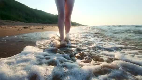 女孩沿着水边走。女人沿着岸边的沙子。摄影机在雌性的后面移动. — 图库视频影像