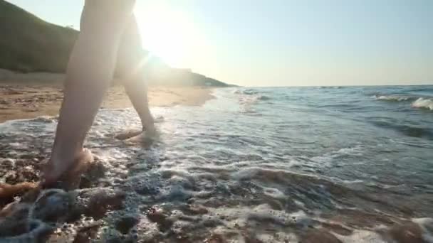 Девушка ходит по краю воды. Женщина идет вдоль берега по песку. Камера движется вслед за женщиной . — стоковое видео