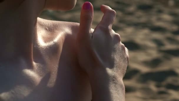 Сексуальная девушка на пляже в черном купальнике смазана солнцезащитным кремом или кремом для загара. Сидит на песке у моря на пляже. Мазки на руках, плечах и ногах — стоковое видео