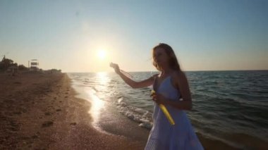 Kız plaj yavaş hareket baloncuklar üfleme. Genç bir kız akşamları, gün batımı sırasında sabun köpüğü darbeler. Plaj boyunca çalışır, sabun köpüğü güneş ışığında sinek..