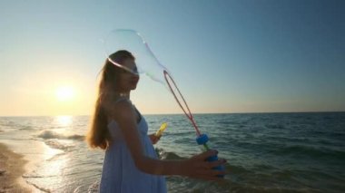 Kız plaj yavaş hareket baloncuklar üfleme. Genç bir kız akşamları, gün batımı sırasında sabun köpüğü darbeler. Plaj boyunca çalışır, sabun köpüğü güneş ışığında sinek..