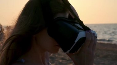 Genç kadın, sahilde bir sanal gerçeklik gözlük kullanır. Seksi kız yaz deniz arka plan üzerinde Vr-kulaklık kullanarak deneyim elde.