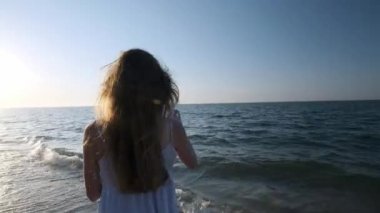 Kız plaj yavaş hareket baloncuklar üfleme. Genç bir kız akşamları, gün batımı sırasında sabun köpüğü darbeler. Plaj boyunca çalışır, sabun köpüğü güneş ışığında sinek.