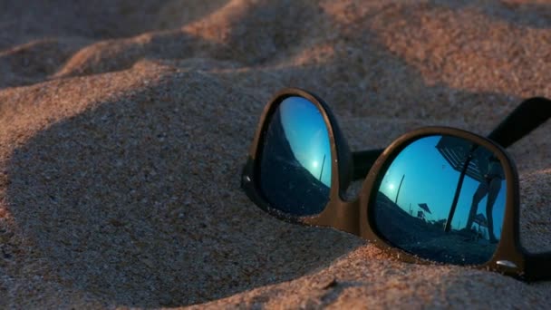 Punti distesi sulla sabbia. Negli occhiali da sole riflettevano il sole, il cielo e la donna che camminava sulla spiaggia. una giovane ragazza sta camminando lungo la spiaggia. Riflesso in occhiali da sole . — Video Stock