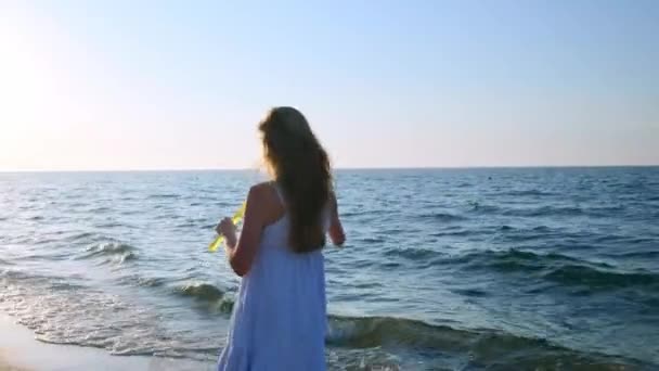 Flicka blåser bubblor på stranden i slow motion. En ung flicka blåser såpbubblor på kvällen under solnedgången. Löper längs stranden, såpbubblor flyger i solljus. — Stockvideo