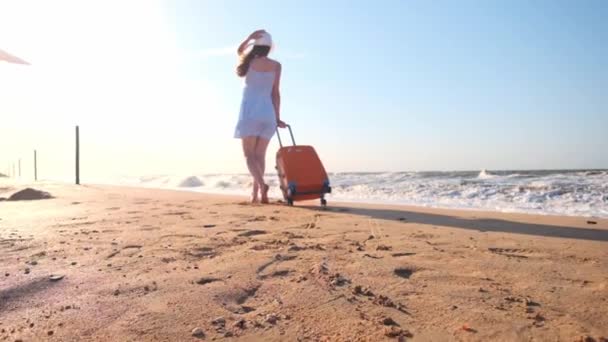 Sahilde oturan bir bavul olan kadın. Genç bir kız plajda bir tekerlekli bavul ile yürür. Kum deniz boyunca boyunca üreticisidir. Kız kendini ve macera arıyor. — Stok video