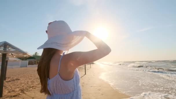 Menina sexy olhando para o mar. Uma rapariga de chapéu e óculos procura um olhar para o oceano. Uma esquerda, perdida. . — Vídeo de Stock