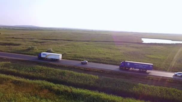 4k-Antenne: Hoch über Container-Sattelschlepper, die an einem schönen Sommerabend Waren auf der vielbefahrenen Autobahn durch das Land transportieren. Autofahren und Raser auf viel befahrener Autobahn bei goldenem Sonnenuntergang — Stockvideo