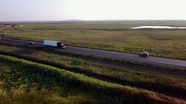 4K AERIAL: volando in alto sopra container semi camion che trasportano merci su strada trafficata in tutto il paese in bella serata estiva. Traffico di guida e di eccesso di velocità in autostrada occupato al tramonto d'oro — Video Stock