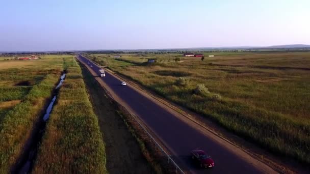 4K AERIAL: Flying high above container semi truck transporting goods on busy highway across the country in beautiful summer evening. Traffic driving and speeding on busy freeway at golden sunset — Stock Video