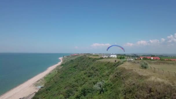 Vista aérea. El parapente vuela sobre la costa. El ala del parapente es soplada por el viento. Fila de mar y bosque . — Vídeos de Stock