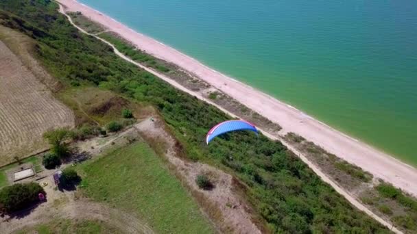 Flygfoto. Paraglider flugor över kusten. Vingen av paraglider blåsas av vinden. Rad av hav och skog. — Stockvideo