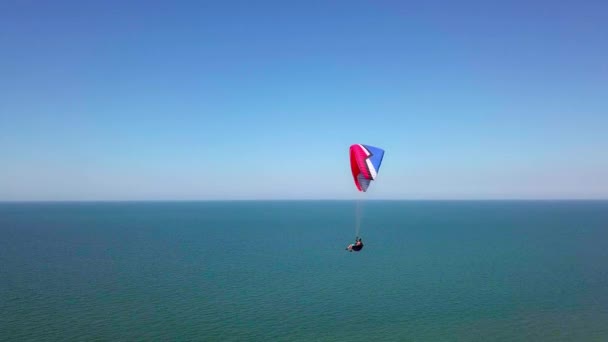 Luchtfoto. De paraglider vliegt over de kustlijn. De vleugel van de paraglider wordt geblazen door de wind. Rij van zee en bos. — Stockvideo