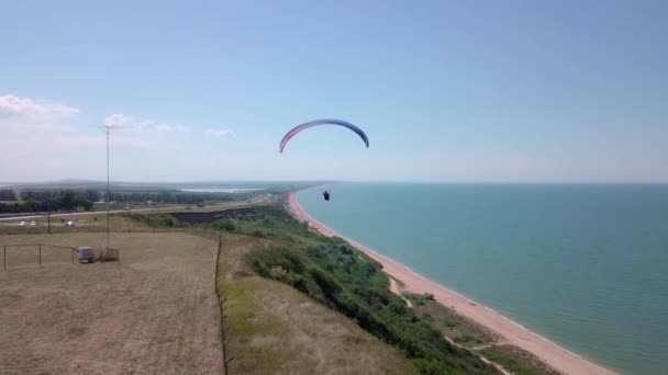 Vista aérea. El parapente vuela sobre la costa. El ala del parapente es soplada por el viento. Fila de mar y bosque . — Vídeos de Stock