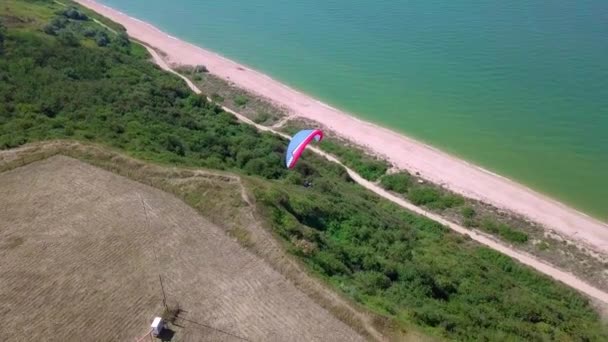 Vista aérea. O parapente voa sobre a costa. A asa do parapente é soprada pelo vento. Fila de mar e floresta . — Vídeo de Stock