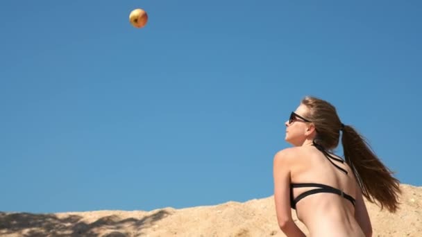 Cámara lenta: Chica joven y sexy en traje de baño negro y gafas, destruye frutas y verduras con un bate de béisbol. Se encuentra en una playa de arena cerca del mar en verano. Rompe la manzana . — Vídeos de Stock