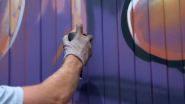 Bir kutu boya ile genç bir adam duvara grafiti çizer. Bir yandan yakın çekim.