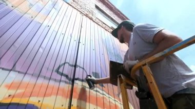 Düşük bir görünümü: bir genç erkek sanatçı bir duvara grafiti boya çizer. Bu bir inşaat kule üzerinde olmalıdır. Sanat yapan bir adam.