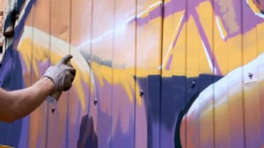 Bir kutu boya ile genç bir adam duvara grafiti çizer. Bir yandan yakın çekim.