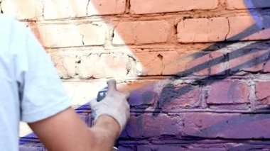 Bir kutu boya ile genç bir adam duvara grafiti çizer. Bir yandan yakın çekim.