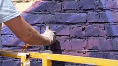 Bir kutu boya ile genç bir adam duvara grafiti çizer. Bir yandan yakın çekim.