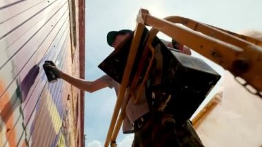 Düşük bir görünümü: bir genç erkek sanatçı bir duvara grafiti boya çizer. Bu bir inşaat kule üzerinde olmalıdır. Sanat yapan bir adam.