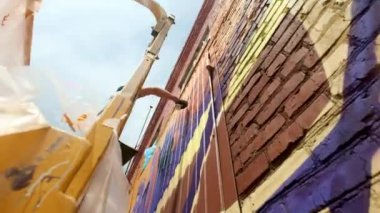 Düşük bir görünümü: bir genç erkek sanatçı bir duvara grafiti boya çizer. Bu bir inşaat kule üzerinde olmalıdır. Sanat yapan bir adam.