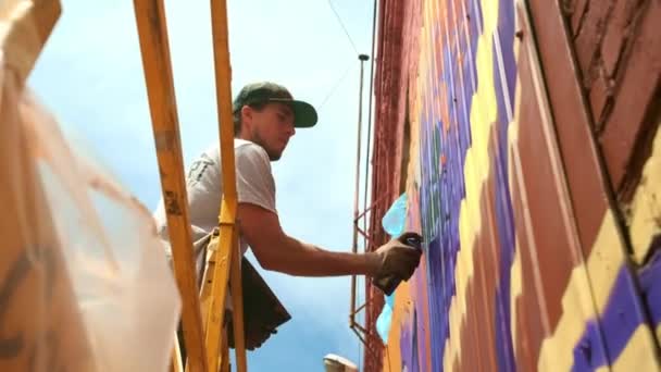 Vista bassa: Un giovane artista di sesso maschile disegna una lattina di pittura a graffiti su una parete. Dovrebbe essere su una torre di costruzione. Un uomo impegnato nell'arte . — Video Stock