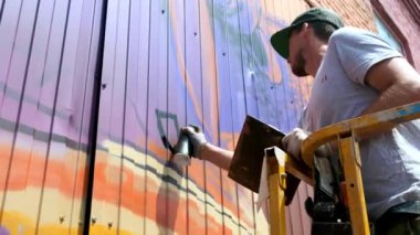 Düşük bir görünümü: bir genç erkek sanatçı bir duvara grafiti boya çizer. Bu bir inşaat kule üzerinde olmalıdır. Sanat yapan bir adam.