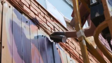 Düşük bir görünümü: bir genç erkek sanatçı bir duvara grafiti boya çizer. Bu bir inşaat kule üzerinde olmalıdır. Sanat yapan bir adam.