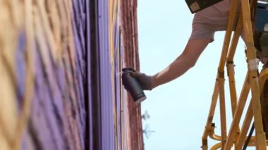 Düşük bir görünümü: bir genç erkek sanatçı bir duvara grafiti boya çizer. Bu bir inşaat kule üzerinde olmalıdır. Sanat yapan bir adam.
