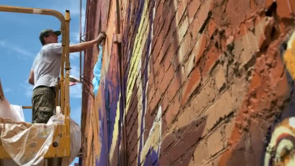 Vista bassa: Un giovane artista di sesso maschile disegna una lattina di pittura a graffiti su una parete. Dovrebbe essere su una torre di costruzione. Un uomo impegnato nell'arte . — Video Stock