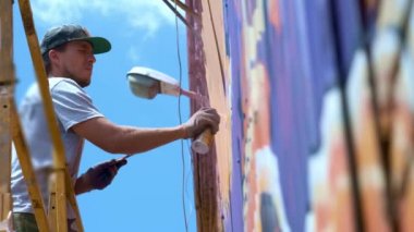 Düşük bir görünümü: bir genç erkek sanatçı bir duvara grafiti boya çizer. Bu bir inşaat kule üzerinde olmalıdır. Sanat yapan bir adam.