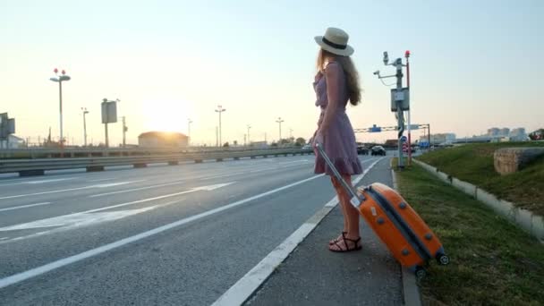 Fata merge pe drum cu o valiză. Aproape de autostradă și multe mașini .. — Videoclip de stoc