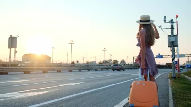 Ragazza va in viaggio con una valigia. Vicino all'autostrada e un sacco di auto .. — Video Stock