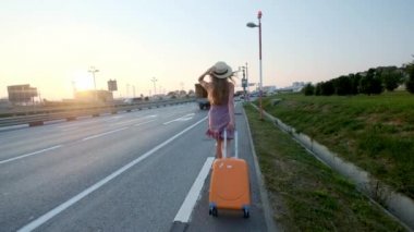 kız bir çanta ile yola devam ediyor. Karayolu ve bir sürü araba yakın.