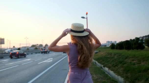 Flicka går på vägen med en resväska. Nära motorvägen och en massa bilar.. — Stockvideo