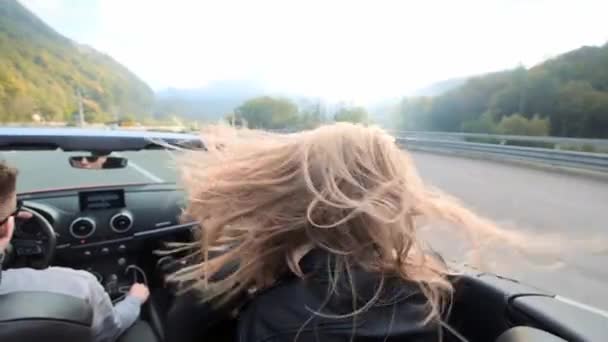 Zwei schöne junge Mädchen fahren in einem roten Cabrio durch die Berge. Straße auf der Autobahn. bekleidet mit schwarzen Lederjacken. Haare flattern im Wind. Reisen und Freiheit genießen. — Stockvideo