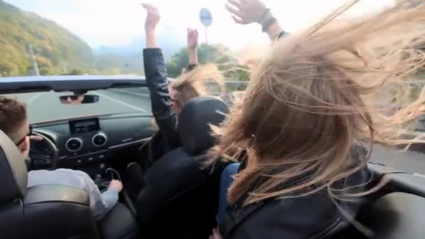 Две красивые молодые девушки ездят в красной кабриолете среди гор. Дорога по шоссе. Одетые в черные кожаные куртки. Волосы трепещут на ветру. Наслаждайтесь путешествиями и свободой . — стоковое видео