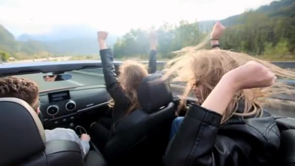 Zwei schöne junge Mädchen fahren in einem roten Cabrio durch die Berge. Straße auf der Autobahn. bekleidet mit schwarzen Lederjacken. Haare flattern im Wind. Reisen und Freiheit genießen. — Stockvideo