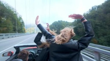 İki güzel genç kızlar arasında dağlar kırmızı bir Cabriolet binmek. Yol karayolu üzerinde. Siyah deri ceket giymiş. Rüzgarda çırpınan saç. Seyahat ve özgürlük keyfini çıkarın.