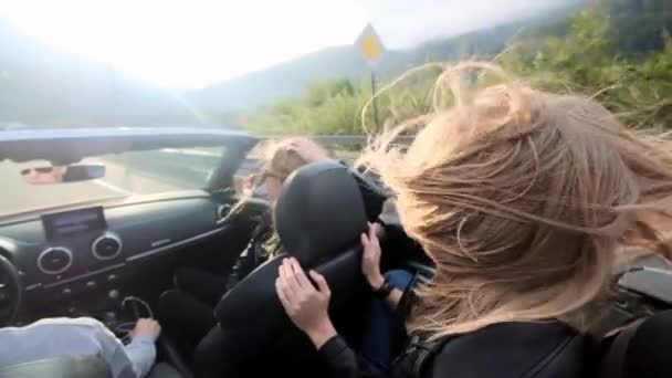 Två vackra unga flickor rida i en röd cabriolet bland bergen. Vägen på motorvägen. Klädd i svart läderjackor. Hår fladdrar i vinden. Njut av resor och frihet. — Stockvideo